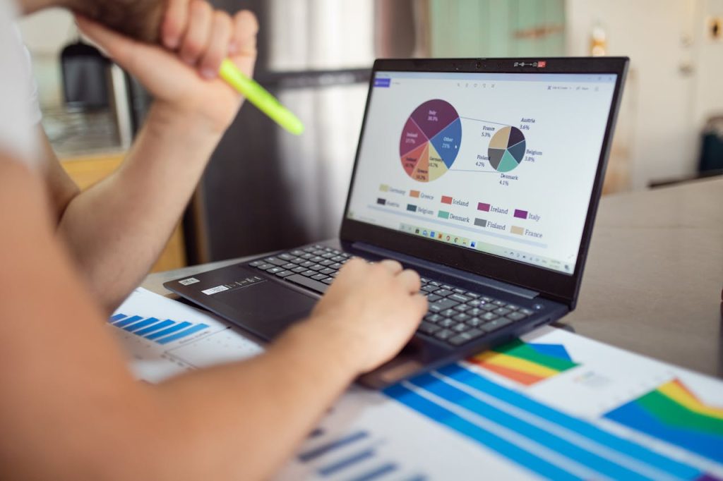 pexels-photo-7948060 Person analyzing financial charts and graphs on a laptop with colorful documents, showcasing market analysis.